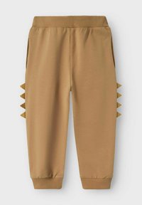 Pruunist puuvillast joggers, millel on elastne vöökoht, küljetaskud ja kolmnurkse aktsendiga detailid hemmi lähedal. Üksikute varrukate lõpetused on kinnitatud pahkluude juures.