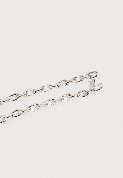 Srebrny łańcuszek z owalnymi ogniwami i małym zapięciem na haczyk na jasnoszarym tle.