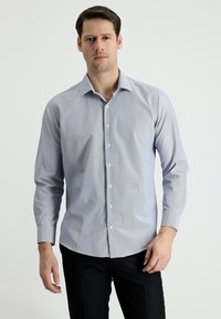 Camicetta azzurro chiaro a maniche lunghe con strisce bianche, colletto con bottoni e orlo curvo, realizzata in tessuto liscio. Dettagli dei bottoni visibili.