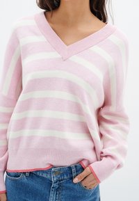 Pull rayé rose et blanc avec un décolleté en V, des manches longues et un ourlet côtelé. Texture douce, agrémentée d'une touche de corail aux poignets.