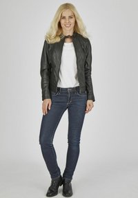 Schwarze Lederjacke mit hohem Kragen, getragen über einem weißen T-Shirt, kombiniert mit dunkelblauen Jeans und schwarzen Stiefeletten; einfaches Design und figurbetonte Passform.