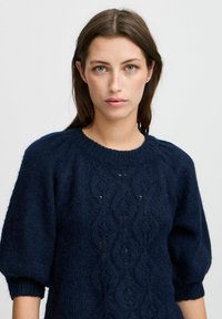 Dunkelblauer gestrickter Pullover mit kurzen Puffärmeln, ausgestattet mit einem strukturierten Rautenmuster sowie einem gerippten Halsausschnitt und Bündchen.