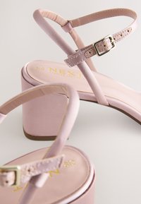 Sandali con tacco in satin rosa con tacco a blocco, caratterizzati da sottili cinturini alla caviglia e dettaglio con fibbia dorata. La soletta mostra il marchio "NEXT".