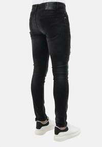 Slim-fit zwarte jeans van denim, met achterzakken, subtiele vervaging en een label op de tailleband. Gecombineerd met witte sneakers.