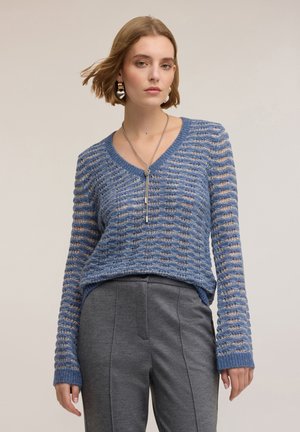 Maglione blu a maglia con scollatura a V, caratterizzato da un motivo a righe testurizzato. Include maniche lunghe e una vestibilità ampia, abbinato a pantaloni grigi.