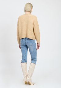 Beige gestrickter Pullover, kurzes Design, weiche Textur; kombiniert mit hellblauen Skinny-Jeans und hochglänzenden beigen kniehohen Stiefeln.
