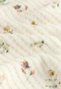 Strukturiertes, cremefarbenes Gewebe mit einem gerippten Muster. Kleine Blumenmuster in Pink, Gelb und Blau über das Material verteilt.