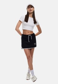 Zwarte shorts met witte zijaccenten en een trekkoord in de taille, gecombineerd met een witte crop top. Model draagt een witte pet en sneakers.