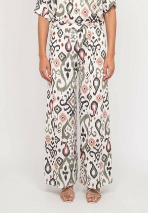 Pantalon taille haute à jambes larges avec une base blanche et des motifs géométriques abstraits en gris, noir et rose, porté avec des sandales à lanières.