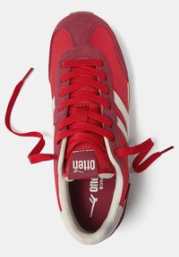 Baskets de sport rouges avec un mélange de daim et de matériaux en tissu. Elles présentent des lacets rouges bien visibles, des accents blancs et une semelle texturée.