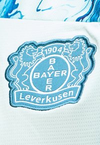 Μπλε και λευκό σήμα Bayer Leverkusen με δύο λιοντάρια και το έτος 1904 σε λευκό υφασμάτινο φόντο με υφή.