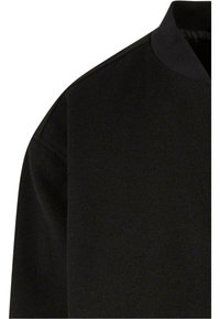 Top negro de cuello redondo con una textura suave y un corte relajado. Presenta costuras sutiles en los hombros y un diseño minimalista.