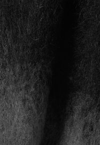 Tissu en laine noir, texturé, avec un aspect doux et duveteux. La surface est inégale, présentant des teintes variées de gris foncé et de fibres noires.