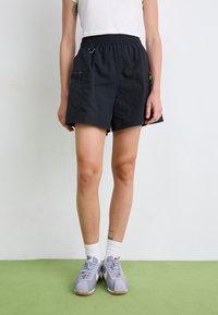 Black lightweight shorts with an elastic waistband, side zippers, and a small carabiner. Paired with gray sneakers and white socks.