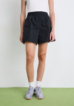 Black lightweight shorts with an elastic waistband, side zippers, and a small carabiner. Paired with gray sneakers and white socks.