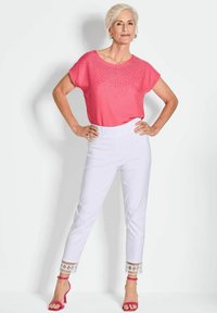 Roze T-shirt met korte mouwen en strass-details, gecombineerd met witte broek met patroon aan de manchetten. Model draagt roze hakken.