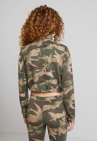 Camo-mönstrad kort sweatshirt och matchande leggings i grönt, brunt och beige. Mjuk tyg, figurnära design, med elastisk fåll.