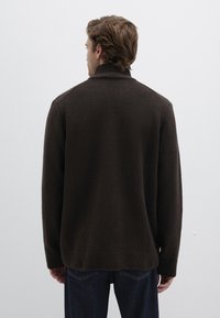 Dunkelbrauner, strukturierter Pullover mit hohem Kragen und langen Ärmeln, von hinten gesehen, kombiniert mit blauen Jeans. Minimalistisches Design.