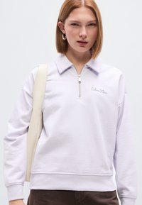 Φούτερ με φερμουάρ σε λιλά χρώμα, με ψεύτικο γιακά, κεντημένο λογότυπο της μάρκας στο στήθος και απαλή, απαλή υφή. Διακοσμημένο με μπεζ λουρί.