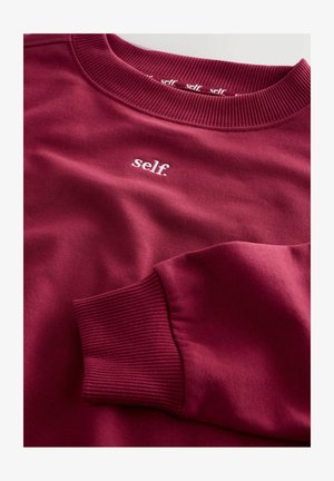 Burgundy sweatshirt med ribbad halsringning och muddar. Har en liten vit "self." logotyp på bröstet. Mjuk bomullsblandning.