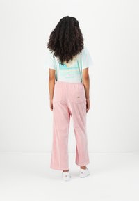 Pantaloni a gamba larga a righe rosa con vita elastica e due tasche sul retro, abbinati a una t-shirt verde menta e scarpe bianche. Sfondo semplice.