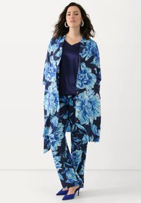 Bloemendessins-outfit met een marineblauwe achtergrond en grote blauwe bloemen, gecombineerd met een blauwe mouwloze top en blauwe hakken.