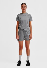 Grå sportoutfit bestående av en kortärmad topp och shorts, tillverkade av andningsbart material, med en logotyp på framsidan. Svarta detaljer.