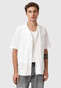 Hvid kortærmet skjorte i letvægtigt stof med knaplukning foran. Den har en afslappet pasform og glat tekstur, kombineret med grå jeans.