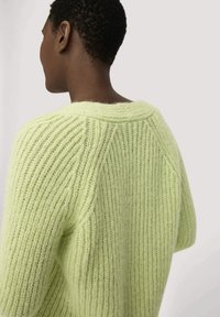 Übergroßer, gerippter Pullover aus weichem, hellgrünem Garn mit weitem Halsausschnitt und überschnittenen Schultern, der eine strukturierte Oberfläche aufweist.