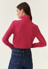 Maglione a maniche lunghe aderente a collo alto in tessuto a coste di un vivace colore rosa, abbinato a jeans in denim scuro a vita alta con tasche posteriori.