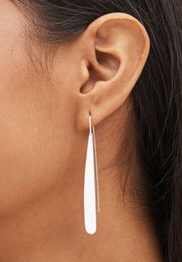 Boucles d'oreilles pendantes en argent avec une forme ovale longue et allongée, surface texturée, suspendues à un crochet fin.