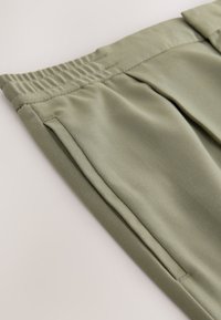 Light olive green trousers featuring a elastic waistband, side pockets, and a smooth, textured fabric with a tailored appearance.