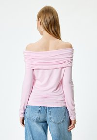 Rosa, schulterfreies Oberteil mit langen Ärmeln, gerafftem Ausschnitt und weicher Textur, kombiniert mit hellblauen, weit geschnittenen Jeans.