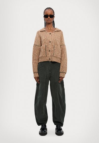 Textureret, tan strikket cardigan med krave, store knapper og forlommer, parret med mørkegrønne breddebukser og sorte plateau sneakers.
