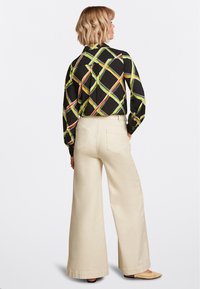 Zwarte shirt met een geometrisch patroon in groen, oranje en geel; gecombineerd met crèmekleurige wijde broek. Textuurstof en minimalistische ontwerpelementen.