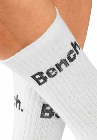 White crew socks with ribbed texture and black printed logo "Bench." on the sides. Soft fabric and fitted ankle design.
