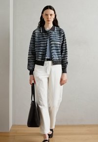 Strikket cardigan med marineblå og hvide vandrette striber, en krave, sorte ribbede manchetter, parret med hvide bukser og en sort tote bag.