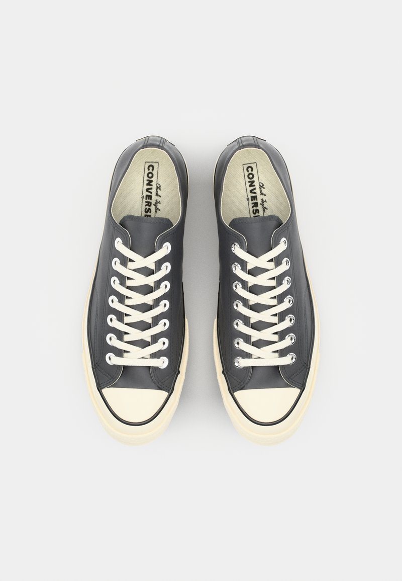 Mørkegrå lærredssneakers med hvide snørebånd, cremefarvede gummitåspidser og en kontrasterende sål. Ingen synlige mønstre eller logoer.