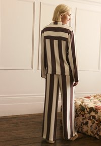 Zweiteiliges Outfit mit einem langärmeligen Oberteil und weitem Hosenbein in vertikalen, dunkelbraunen und cremefarbenen Streifen, aus glattem Stoff gefertigt.