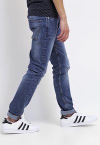 Slim-fit blå denimjeans med en blekt textur, som har fem fickor och uppvikta byxben, i kombination med vita sneakers med svarta ränder.