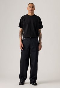 Camiseta de algodón negra con un corte relajado, combinada con pantalones de pierna ancha de color azul oscuro. Los pantalones cuentan con bolsillos laterales y un cierre de botón.