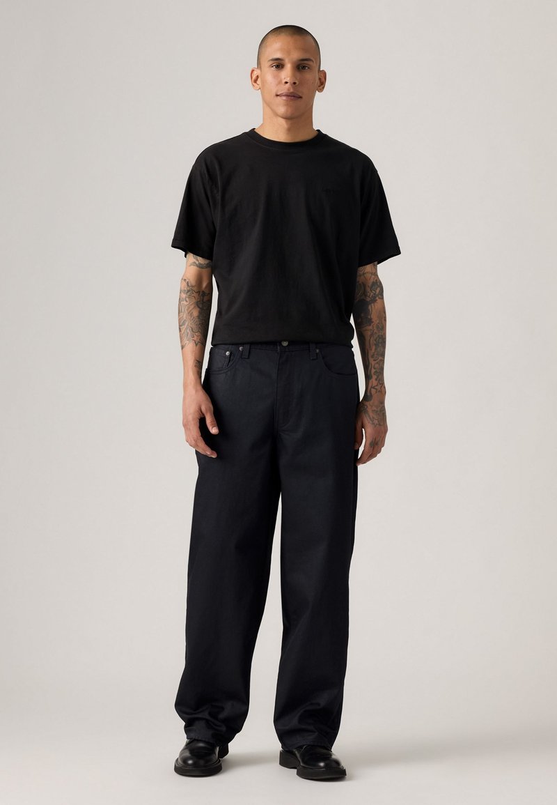 Camiseta de algodón negra con un corte relajado, combinada con pantalones de pierna ancha de color azul oscuro. Los pantalones cuentan con bolsillos laterales y un cierre de botón.
