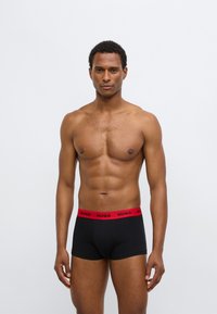 Cuecas boxer pretas com cós elástico vermelho com o logo "HUGO". Material liso e ajustado, concebido para conforto e suporte.