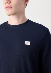 Marineblauwe geribbelde langetermijn t-shirt met ronde hals en een klein rechthoekig Calvin Klein logo flapje op de linkerborst.