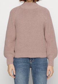 Pull en maille rose clair avec col montant, manches raglan et poignets et ourlet côtelés ; présente un motif en maille épaisse texturée.