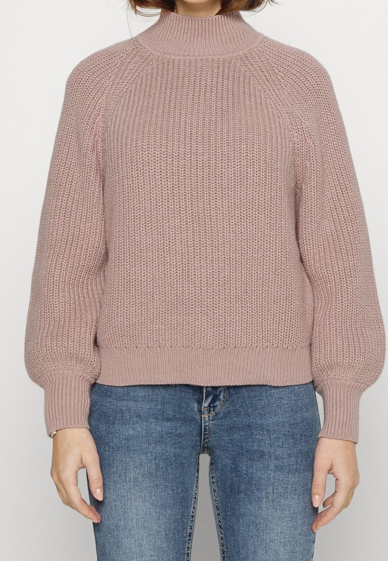 Pull en maille rose clair avec col montant, manches raglan et poignets et ourlet côtelés ; présente un motif en maille épaisse texturée.
