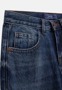 Donkerblauwe denim jeans met een klassiek vijf-pocket ontwerp, voorzien van zichtbare stiksels en een merklabel op de tailleband.
