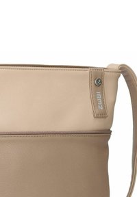 Beige leren handtas met een gladde textuur, voorzien van een ritstasje en een zijkantlabel met de "iamz"-branding in zilver.