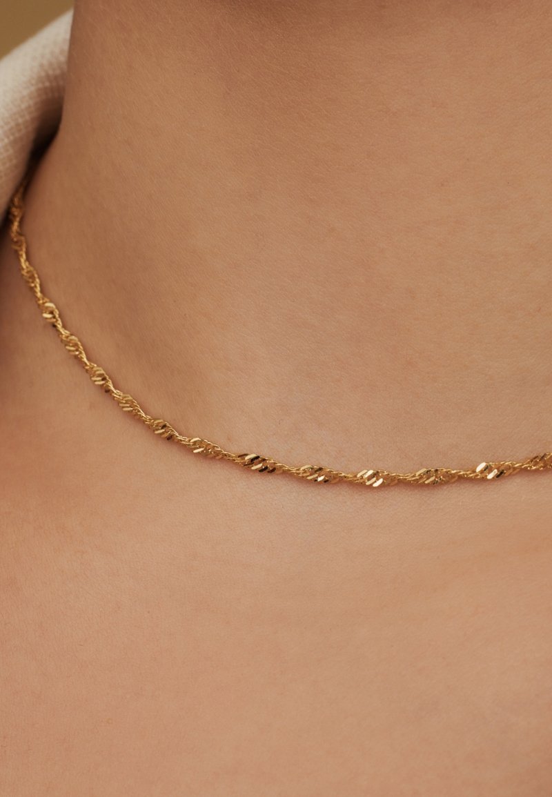 Collier en chaîne à maillons torsadés en or, présentant de petits maillons plats et texturés alternés. Le design suit une forme élégante et continue.