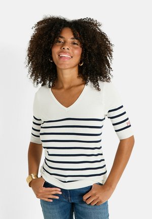 Top de cuello en V a rayas en crema y azul marino, con mangas cortas, textura de punto y detalle del logo rojo en la manga. Llevado con jeans azules.